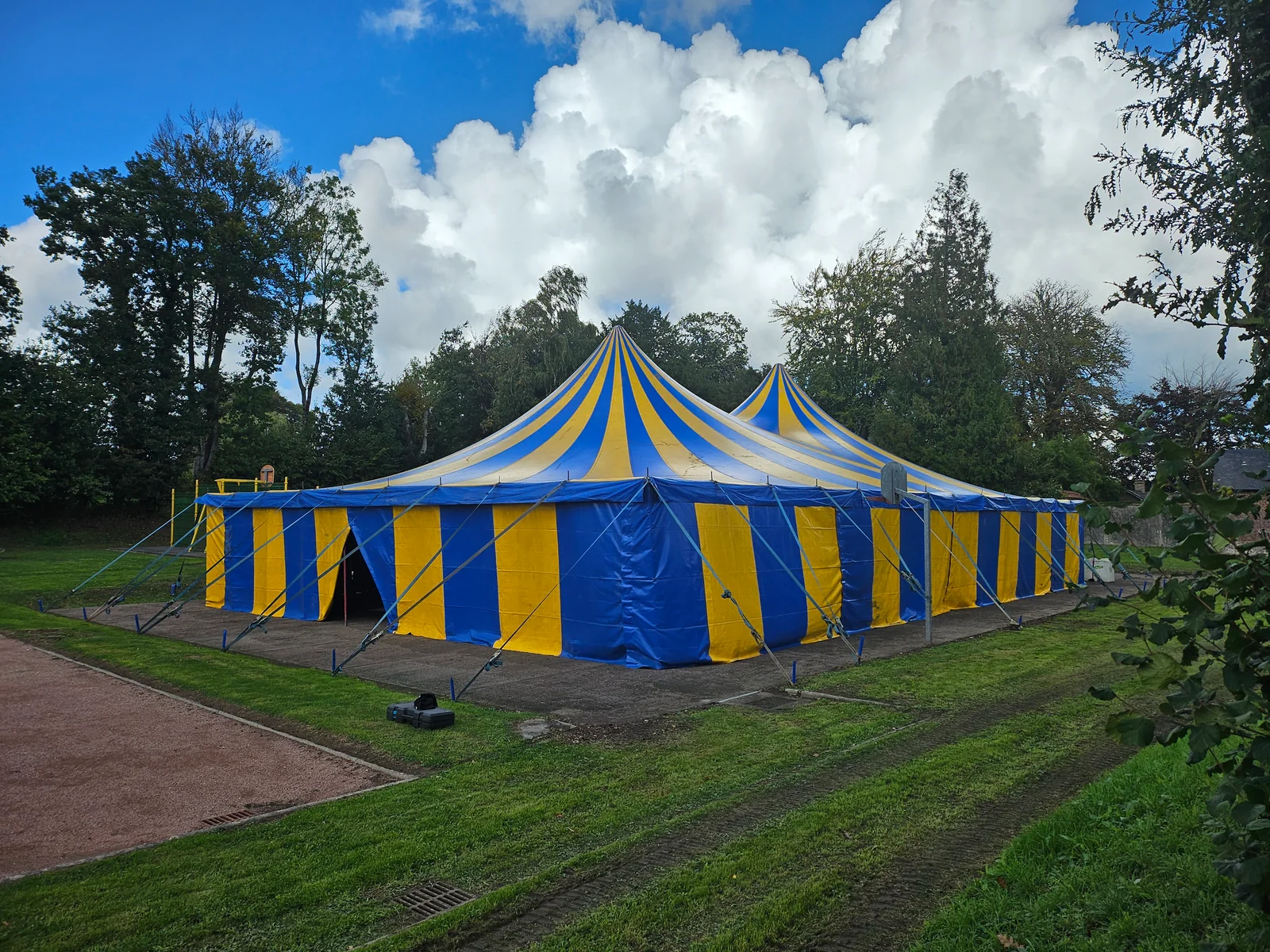 Chapiteau Foyer bleu et jaune, fermé, installé dans un cadre arboré.