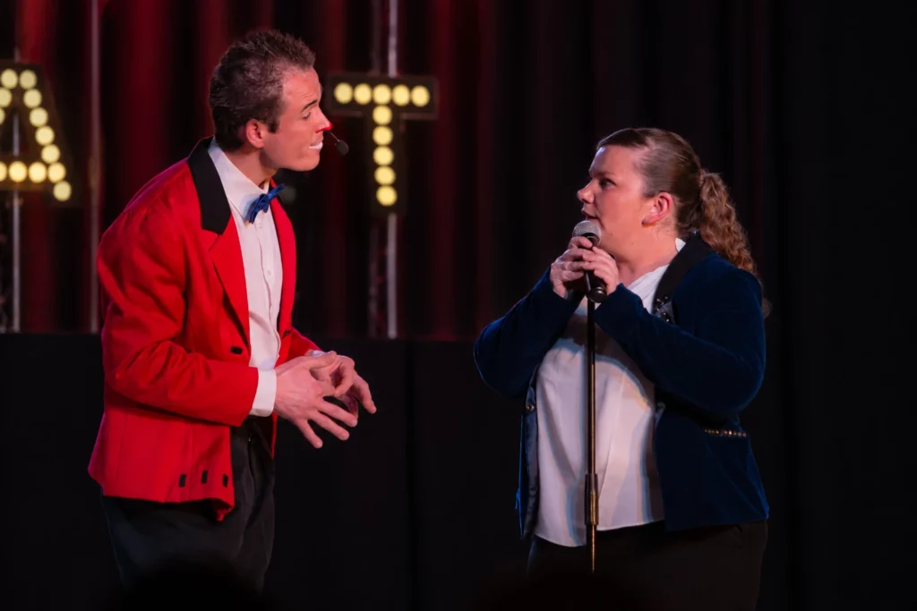 Un duo sur scène : costume rouge, veste bleue et micro.