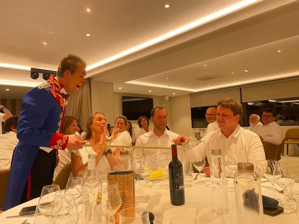 Un artiste en costume bleu propose un mini-verre à un spectateur pendant un repas.