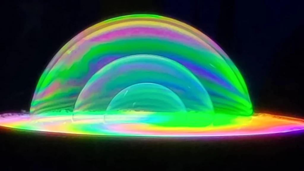 Plusieurs bulles de savon lumineuses aux reflets verts et multicolores.